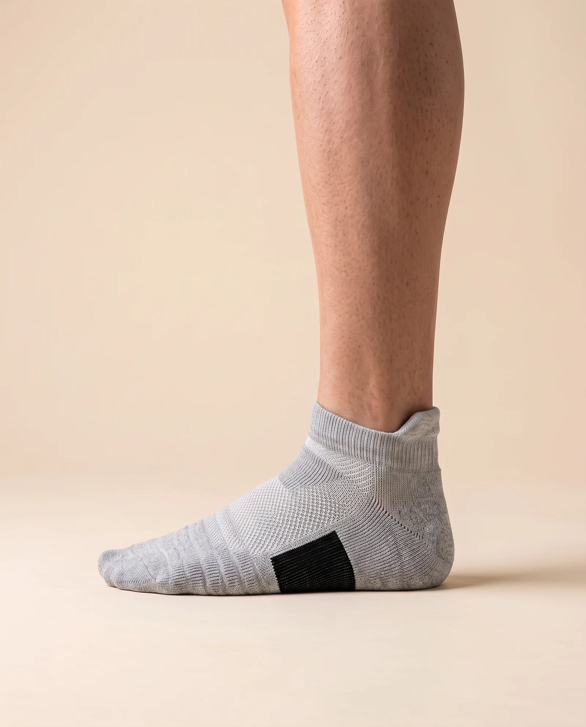 Gray low-cut court sock with black arch panel, worn on foot, side view